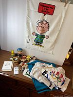 Overview of lot on dresser: towel, pig bank, rattles, Snoopy items, T-shirts