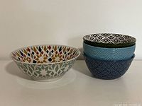 Set of four ceramic bowls including three smaller patterned cereal bowls and one larger multicoloured serving bowl.
