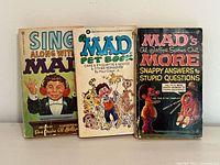 Front view of three MAD Magazine vintage paperback books: Sing Along with MAD, MAD Pet Book, and MAD's Al Jaffee Spews Out More Snappy Answers to Stupid Questions, showing cover artwork and condition.