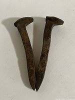 Two vintage railroad spikes positioned side by side showing full length and shape.