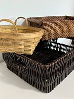 Set of three baskets shown from side angle, featuring one round natural wood basket and two rectangular dark brown wicker baskets stacked.