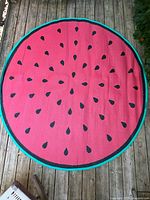 Full view of the rug's red watermelon side showing black seeds and green edge laid on wooden decking.