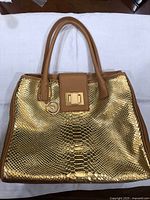 Front view of metallic gold snake-embossed handbag with tan leather trim and handles