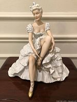 Front view of porcelain ballerina seated, tying shoes
