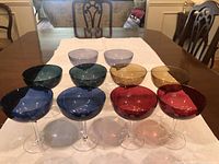 All ten coloured coupe glasses on table runner, showing full set and colour variety