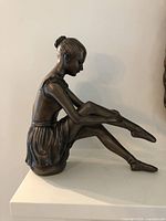 Side view of ballerina figurine showing seated pose and bronze finish