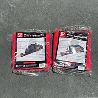 Two Wilson Player's Equipment Bags in red, sealed in original packaging, lying side by side on a gray floor surface.