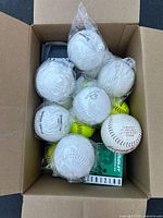 Box containing 15 softballs of white color, some individually wrapped in plastic, showing multiple balls with readable branding.