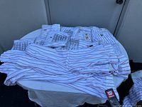 Multiple white men's baseball pants with red pinstripes stacked and laid out, some still in plastic bags showing new condition.