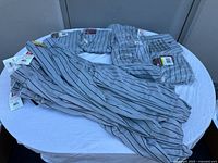 Seventeen pairs of youth baseball pants in grey with black pinstripes, laid out on a table showing tags and details.