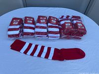 Full view of all 18 pairs of red and white striped socks, some still in original packaging, one pair laid out flat showing stripes and solid toe and heel.