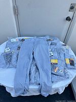 Front view of one pair of blue-grey Wilson baseball pants laid on top of multiple packaged pairs on a table outdoors.
