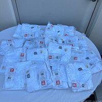 All 20 white youth baseball pants by Wilson, folded and sealed in clear plastic bags, laid out on a table.