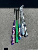 Five aluminum baseball bats laid out with varying colors and brands. One wrapped in plastic.