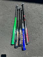 Top view of five aluminum baseball bats grouped together on the ground, showing colors and grips.
