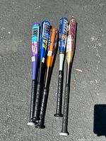 Five aluminum baseball bats arranged vertically on pavement, showing the handles and branding.