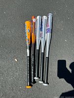 Full group top view of five aluminum baseball bats arranged parallel outdoors on pavement showing grips and barrel logos.