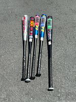 Five Easton aluminum baseball bats laid on asphalt, showing grips and barrel logos.