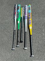 Five Easton aluminum baseball bats laid out on pavement showing model names and grips, variety of colors including silver, green, black, and gold.