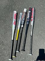 Top view of all 5 aluminum baseball bats laid side by side showing brand decals and grip condition