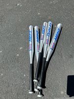 Five Dudley aluminum bats laid on pavement, showing full length and grips