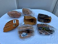 Seven Franklin brand leather baseball gloves on a white surface. Some gloves are wrapped in plastic. The gloves are tan and brown shades, marked RTP Series.
