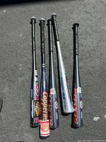 Top view of five baseball bats lined up on pavement showing full length and grips.