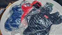 Four Rawlings catcher's pads in black, red, and blue colors, still sealed in plastic bags on a white surface.
