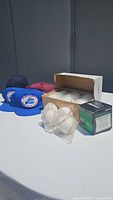 Lot includes five baseball caps placed in front and behind a box of softballs, along with individually wrapped baseballs and a green Dudley softball box.