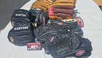 Overview of all 9 baseball mitts arranged on a white table showing mix of Easton, Wilson, and Rawlings brands, black and tan colors.