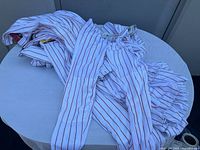 Group of folded men's baseball pants shown on table, all white with red vertical stripes, some elastic waistbands partially visible.