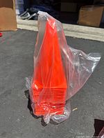 Stack of bright orange short practice cones wrapped in clear plastic, visible in outdoor lighting.
