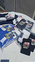 Multiple pairs of packaged sports socks in black, blue, and white, arranged on a white surface outdoors.
