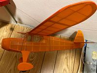 Left front view of orange high-wing model airplane suspended by wire