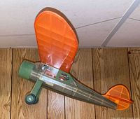 Left side view of green fuselage and orange wing/tail model plane on wood floor