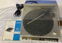 Turntable with closed dust cover, power cord coiled, owner’s manual visible