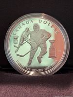 Front side of the silver dollar coin depicting two hockey players, the Stanley Cup, and inscriptions
