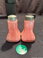Pair of pink cased glass salt and pepper shakers with metal tops, showing general front view and shape with embossed patterns.