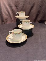 Three demitasse cup and saucer sets arranged in a staggered vertical line on black surface and dark background.