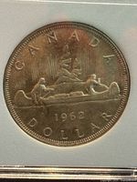 Close-up of the reverse side of the coin showing the Voyageur canoe with two figures and the date 1962 with 'CANADA DOLLAR' around the edge.