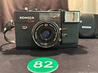 Front view of Konica C35 EF camera featuring branded Hexanon 38mm f2.8 lens, textured grip, flash unit, and controls