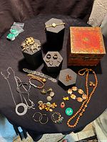 Top view of assorted jewelry pieces including rings, brooches, earrings, bracelets and necklaces, displayed on a table around black display stands and small bags.