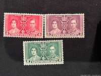 Three Newfoundland postage stamps from 1937 Royal Visit, showing King George VI and Queen Elizabeth in red, purple, and green colors.
