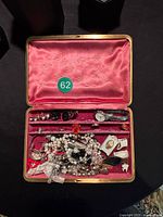 Opened red satin-lined jewellery box showing assorted items in upper and lower trays