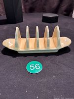 Yellow ceramic toast rack with five slots, photographed from an angled side view showing the curved handles and slots.