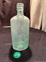 Side view of the clear aqua glass bottle embossed with "GORDON'S DRY GIN" showing the shape and condition.