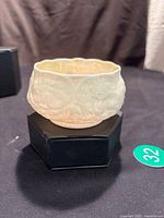 White porcelain sugar dish with embossed floral pattern and scalloped rim sitting on a black stand.