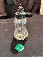 Full view of the ribbed glass sugar shaker with silver top on a dark surface.