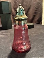 Full view of cranberry glass sugar shaker with silver plated lid, showing shape and color.