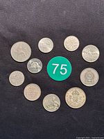 Top view showing 10 various world coins and tokens arranged on black background with green number 75 tag.